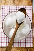 Mozzarella with brine in glass bowl and on wooden spoon