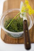 Dill in glass bowl with dill flowers on chopping board
