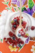Fresh berries in jam jar with sugar and wooden spoon