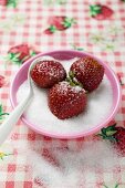Three strawberries in a small dish of sugar