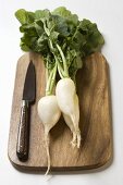 Icicle radishes with leaves & knife on chopping board