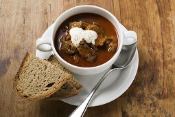 Goulash soup with sour cream in soup cup, slices of bread