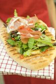 Woman holding pizza bread topped with Parma ham, herbs, chilli rings