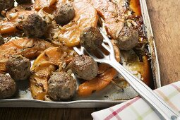 Meatballs with roasted pumpkin wedges on baking tray