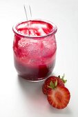 Glas Erdbeermarmelade mit Löffel, daneben frische Erdbeeren