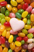 Bunte Jelly Beans und ein zartrosa Zuckerherz (bildfüllend)