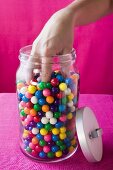 Hand reaching into jar of coloured bubble gum balls