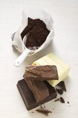 Cocoa powder in bag with scoop, pieces of chocolate beside it