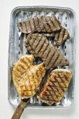 Grilled meat in aluminium grill tray (overhead view)