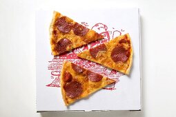 Drei Stücke Pizza mit Peperoniwurst auf Pizzakarton
