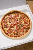 Pizza mit Tomatenscheiben, Käse und Oregano im Pizzakarton