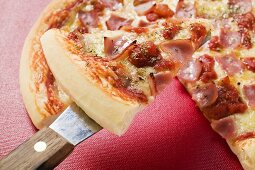 Pizza mit Schinken, Tomaten und Käse mit Stück auf Heber