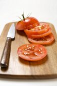 Tomato slices and knife on chopping board