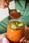 Woman holding preserving jar of tomato sauce and ladle
