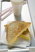 Toasted cheese sandwiches on paper napkin, paper cup, straws