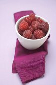 Raspberries in white bowl on purple cloth