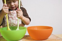 Child stirring bowl with two wooden spoons