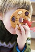 Small boy holding gingerbread tree ornament in front of his face