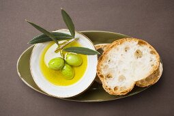 Grüne Oliven am Zweig in Schale mit Olivenöl, Weißbrot