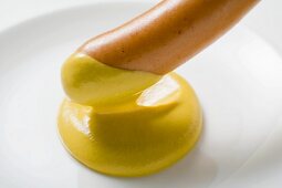 Dipping frankfurter in mustard (close-up)