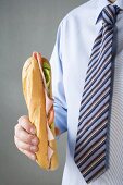 Mann mit Krawatte hält Subsandwich mit Schinken