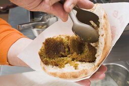 Garnishing pita bread filled with falafel (chick-pea balls)