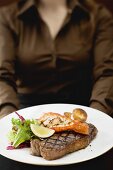 Woman holding plate of Surf & Turf (beef steak with prawn)