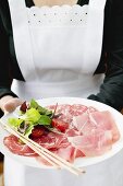 Kellnerin serviert italienische Wurstplatte mit Grissini