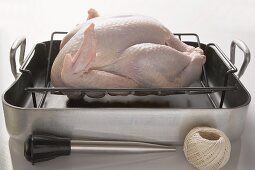 Chicken in roasting tin,  kitchen utensils beside it