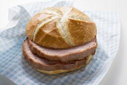 Slices of Leberkäse (type of meatloaf) in a roll on paper napkin