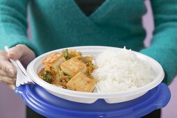 Frau hält Plastikteller mit Tofu, Gemüse und Reis