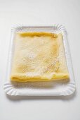 Crêpe with icing sugar on paper plate