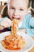 Girl eating ribbon pasta with tomato sauce