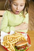 Mädchen betrachtet entsetzt Hamburger mit Pommes frites