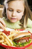 Mädchen isst Pommes frites mit Ketchup und Hamburger