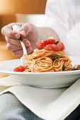Person isst Spaghetti mit Tomaten und Rosmarin