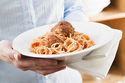 Person hält Teller Spaghetti mit Hackbällchen