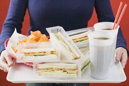 Frau hält Tablett mit Sandwiches, Cola und Chips