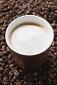Cup of coffee with milk froth on coffee beans