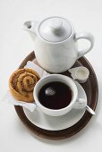 Cup of coffee, cinnamon bun, cream and coffee pot on tray