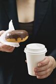 Woman holding doughnut and plastic coffee cup