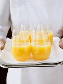 Chambermaid serving several glasses of orange juice on tray