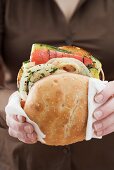 Woman holding toasted roll filled with grilled vegetables