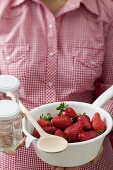 Frau hält Seiher mit Erdbeeren, Marmeladengläser und Kochlöffel