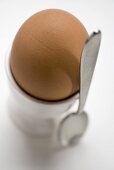 Braunes Ei im Eierbecher, daneben Löffel