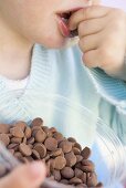 Child eating chocolate buttons out of plastic tub
