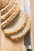 Oat bread, sliced, on chopping board with bread knife