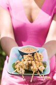 Woman holding platter of satay and peanut dip