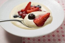 Vanilla cream with berries on spoon over plate