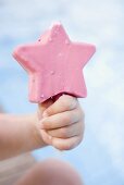 Child's hand holding a pink ice cream on a stick
